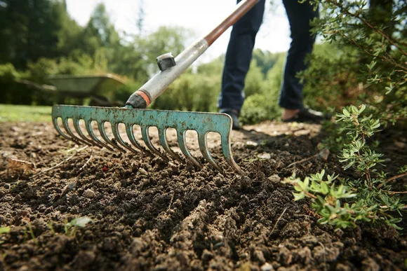 Person harkt Boden mit Gartenharke